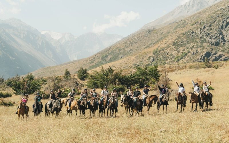 Tour Lab group on horseback, wearing helmets, lined up in a golden meadow in Yerba Loca with the Andes behind them