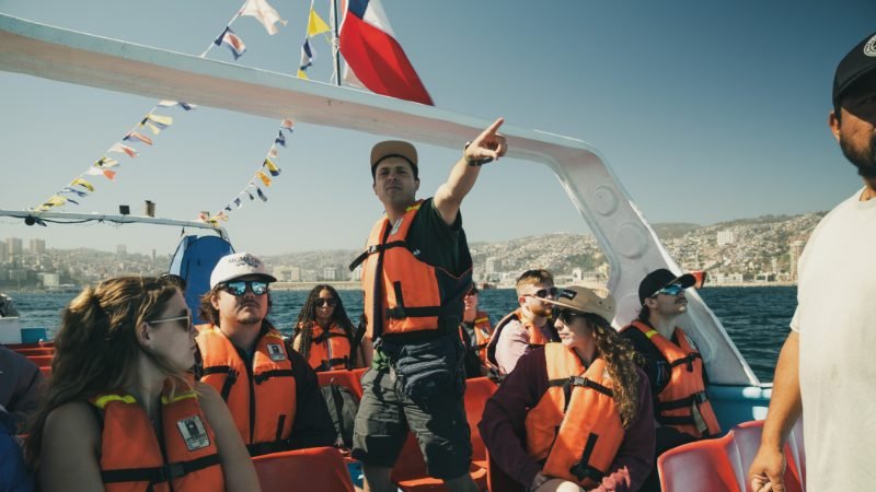 Tour Lab guide pointing out landmarks from the boat with Valparaíso's hillside cityscape behind