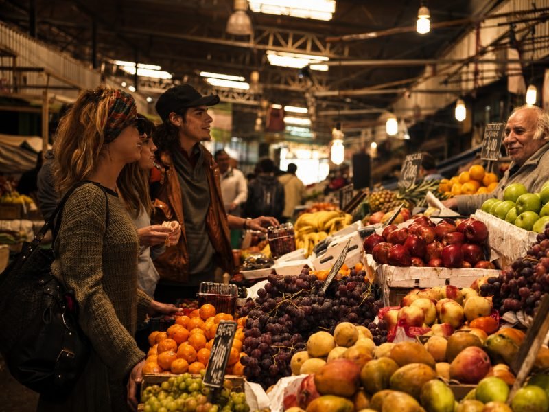 Viajeros comprando frutas con vendedor en La Vega Central de Santiago